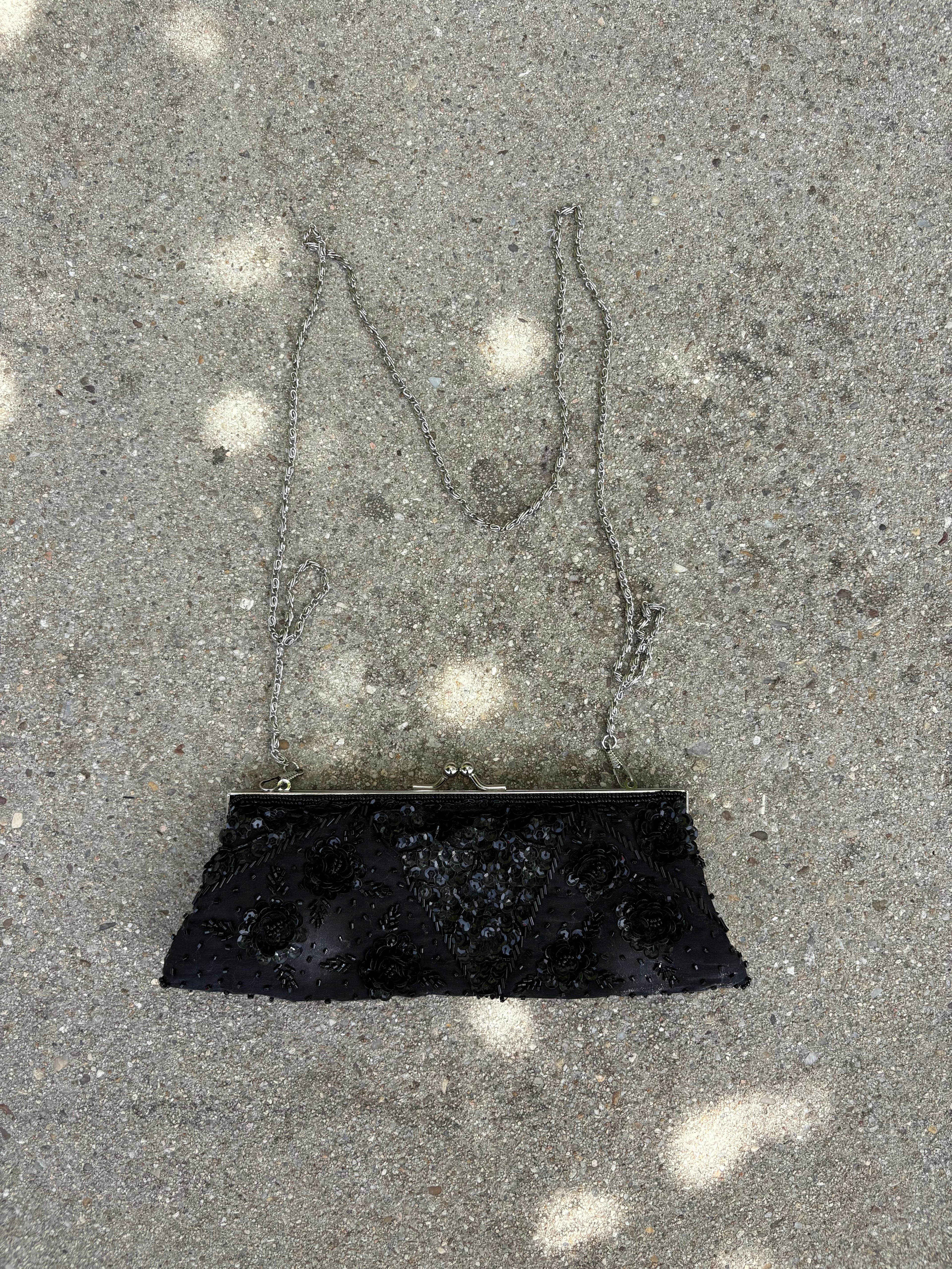 Cartera negra con detalles lentejuela y pedrería flores y cadena metálica plateada